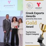 Two-panel social media graphic celebrating Generation Y's Gold Award at the Greek Exports Forum & Awards 2026. The left panel shows a color photograph of three people on the awards stage: a man in a gray suit and two women from the Generation Y team, one in a white blouse and black trousers holding the Gold Award trophy, and one in a white suit. Behind them, a presentation screen displays the "generation Y — international e-business hub" logo. The right panel is a light gray branded layout with the Greek Exports Forum & Awards logo and the Generation Y logo at the top, separated by a vertical divider. Below, bold typography reads "Greek Exports Awards, powered by ethos events," the word "Gold" in large gold lettering, "Award" beneath it, and the category title "Top Services Export Company." A black-and-white image of a hand raising a golden trophy appears on the right edge, with gold horizontal accent bars at the top and bottom. The "Generation Y Team" label and GY arrow icon appear in the lower left corner.